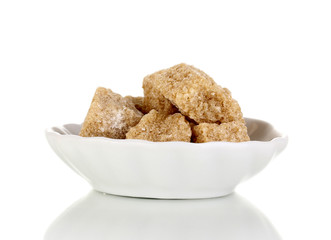 Lump brown cane sugar cubes on saucer isolated on white