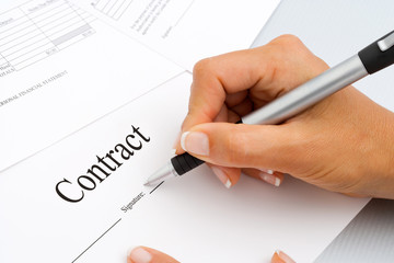 Close up of hand signing contract documents.