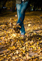 Feet walking through brightly colored fall leaves on the ground.