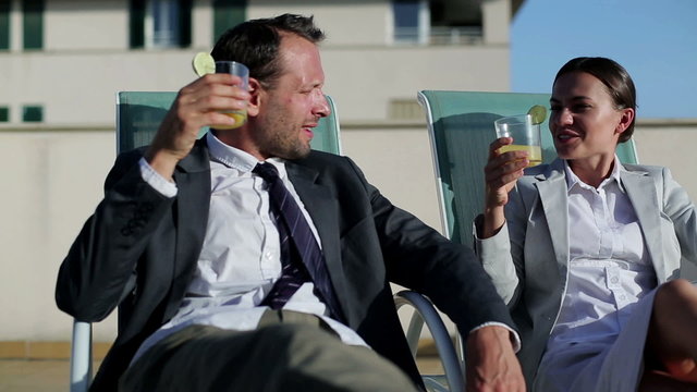 Happy business couple with drinks relaxing on sunbeds