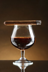 glass of brandy and cigar on brown background