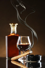 bottle and glass of brandy and cigar on brown background