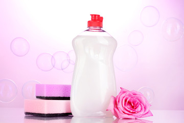 Dishwashing liquid with sponges and flower on pink background