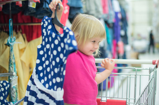 Adorable baby on cart choose clothes in supermarket