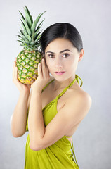 Kobieta w zielonej sukience trzymająca w dłoniach ananasa