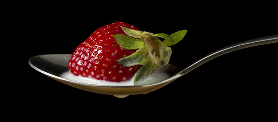 red, ripe strawberry falling in spoon with milk