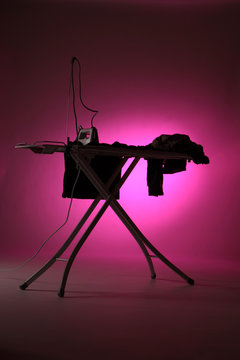Bügelbrett mit Bügeleisen und Kleidung vor lila Hintergrund