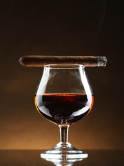 glass of brandy and cigar on brown background