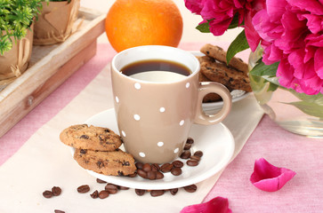 cup of coffee, cookies, orange and flowers on table in cafe