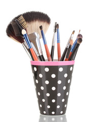 Makeup brushes in a black polka-dot cup isolated on white