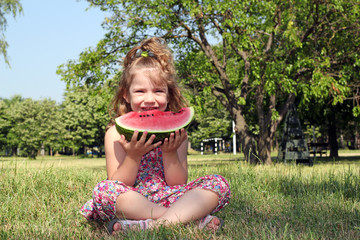 little girl sitting on grass and eat watermelon