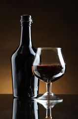 Glass of brandy and bottle on brown background