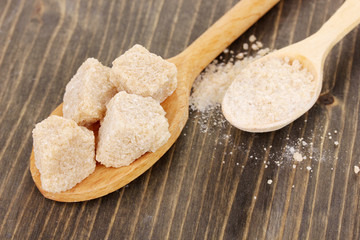 Brown sugar in spoons on wooden background