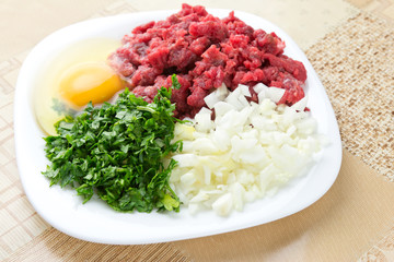 Chopped onion, minced beef, parsley and an egg on plate