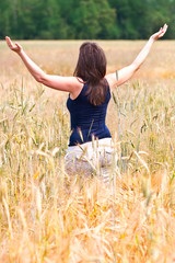 młoda kobieta stojąca w zbożu podnosi ręce do góry