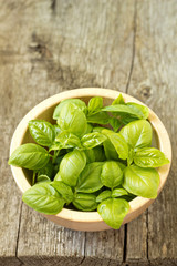 Leaves of fresh basil in a bowl on wooden table