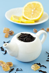 Small tea pot with leaves of black tea, sugar and lemons
