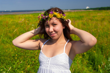 beautiful girl in wreath of flowers in meadow on sunny day