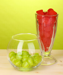 Color candies in glasses on wooden table on green background