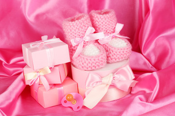 pink baby boots, pacifier, gifts on silk background.