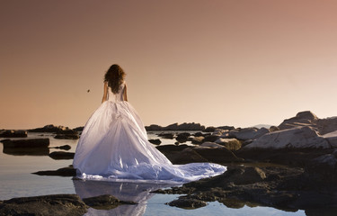 Fototapeta na wymiar Beautiful slim bride in wedding dress on sunset beach near sea
