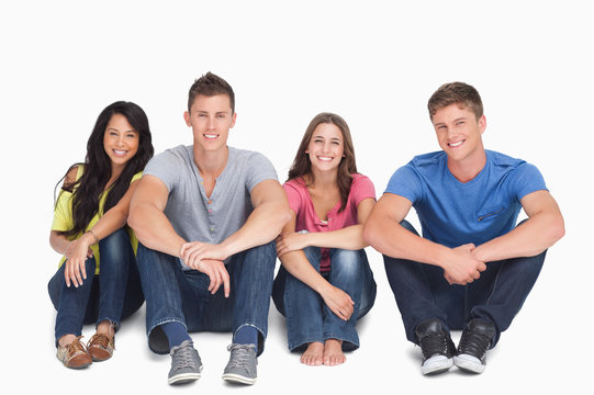 Smiling Group Sitting On The Ground With Their Hands On Their Le