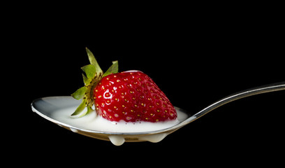 red, ripe strawberry falling in spoon with milk