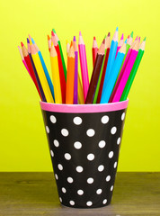 Color pencils in glass on wooden table on green background