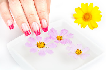 Hands with manicure relaxing in water and flowers