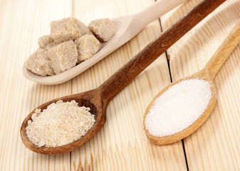 White and brown sugar in spoons on wooden background