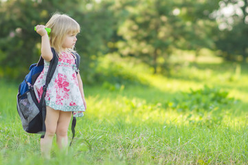 Adorable girl with huge backpack and toy shovel walking in park