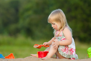 Adorable baby play with small shovel and pail in sand on playgro