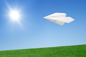 Paper airplane flying over the lawn against the blue sky