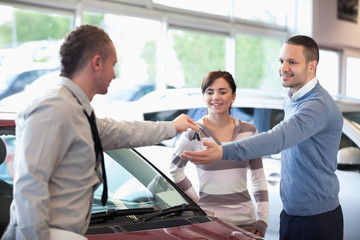 Fototapeta premium Smiling couple receiving keys from a car dealer
