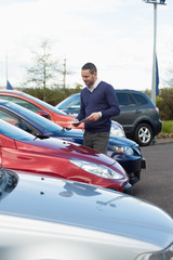 Man looking at a car while holding a file