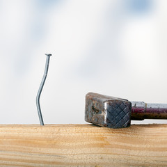 Crooked nail in the wooden board with a hammer