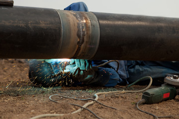 Welder wearing protective clothing lying under pipe welding