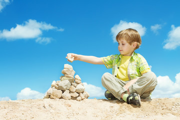 Child putting last stone part to pyramid sitting over sky