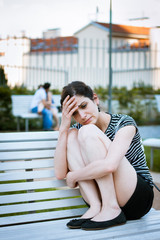 Fototapeta premium Depressed young woman sitting in a park full of happy couples