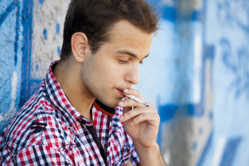 Fototapeta na wymiar Young teen boy smoking near graffiti wall.