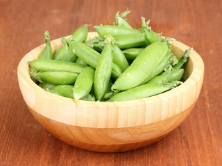 Green peas in wooden bowl on wooden background