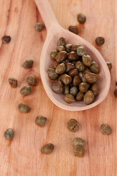 green capers in wooden spoon on wooden background close-up