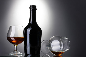 Glasses of brandy and bottle on gray background