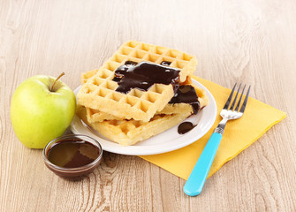 Tasty waffles with chocolate on plate on wooden background