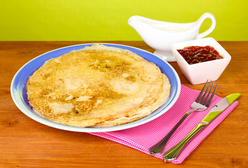 Stack of tasty pancakes on wooden table on green background