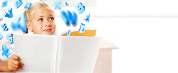Portrait of a young girl in school at the desk. Reading book and