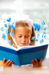 Portrait of a young girl in school at the desk. Reading book and