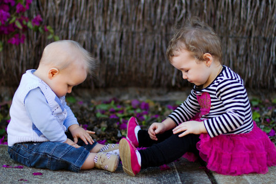 Baby Boy And Toddler Girl Sitting And Playing Outdoors