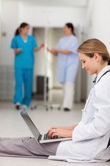 Obraz premium Doctor sitting on the floor while typing on a laptop