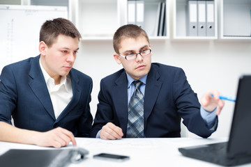 Two young businessmen working together with computer at office